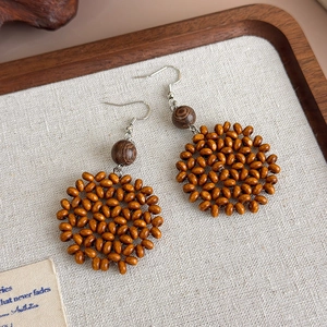 Detail of handmade amber wood bead woven earrings with vintage geometric round pendant