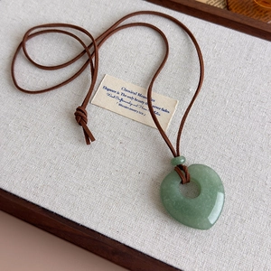 Detail of a heart-shaped green natural stone pendant with a brown suede cord on linen