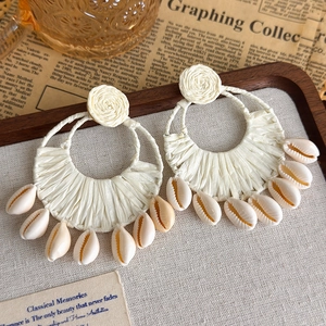 Nahaufnahme von Bohemian Raffia-Ohrringen mit kleinen natürlichen Muschel-Anhängern