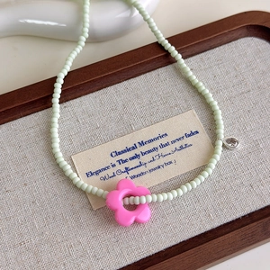 Détail du collier de perles vert menthe avec pendentif fleur rose sur un plateau en bois