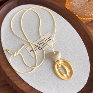 Detail of geometric matte gold oval pendant on a beige adjustable cord necklace