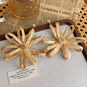 Detailansicht handgefertigter Bast-Blumenohrringe mit Goldsteckgoldenen Steckern auf Holztablett