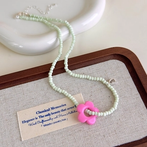 Détail du collier de perles vert menthe avec un pendentif en forme de fleur rose