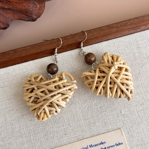 Detailed close-up of handmade woven heart earrings with rustic wooden beads and silver hooks