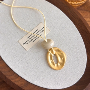 Detail of a geometric irregular gold pendant on a beige cord necklace over a wooden tray
