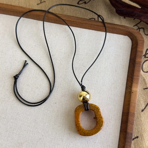 Détail d'un long pendentif ethnique avec perle dorée et anneau en résine ambrée craquelée