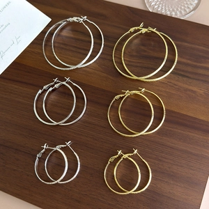 Detailed view of gold and silver textured hoop earrings in three sizes on a wooden tray