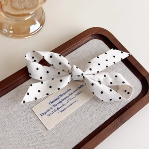Détail d'un nœud papillon blanc à pois noirs posé sur un plateau de présentation en bois