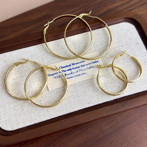 Three-pair set of gold hoop earrings with matte textured finish on a wooden jewelry tray