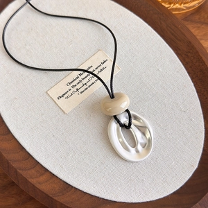 Detailed macro view of the irregular oval metal pendant with a beige bead on black cord