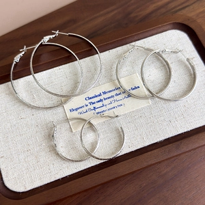 Three pairs of silver hoop earrings with polished and frosted textures on a wooden tray