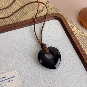 Detail of a polished heart-shaped black stone pendant on a brown cord necklace