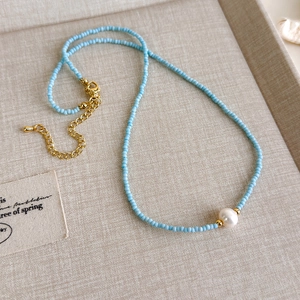 Details einer blauperlenbesetzten Halskette mit weißer Perle und Goldverschluss auf Leinen