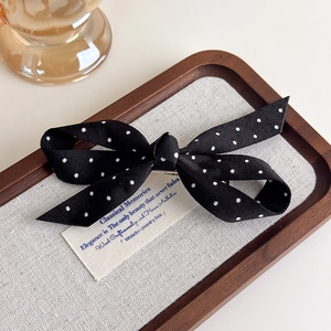 Détail de la pince à cheveux noeud en satin noir à pois blancs sur tissu en lin