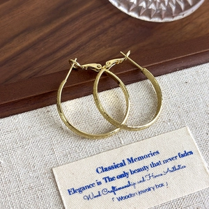 Detailed view of gold hoop earrings with matte textured finish on a fabric background