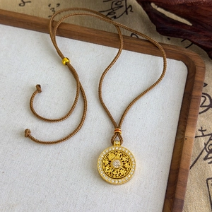 Détail d'un pendentif rond doré évidé avec zircons blancs sur cordon tressé marron
