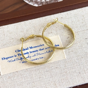 Detailed close-up of gold hoop earrings with a textured sandblasted shimmering surface