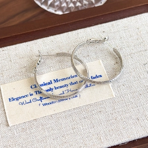 Detail of silver hoop earrings with textured sandblasted finish on a beige background