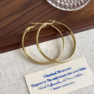 Detail of golden hoop earrings featuring a fine frosted star texture on wooden tray