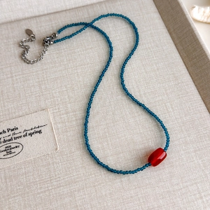 Detail einer blauen Perlenkette mit roter Mittelperle und silbernem Verschluss auf Leinentablett