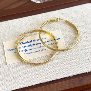 Macro shot of gold textured hoop earrings resting on a rustic linen jewelry box lining