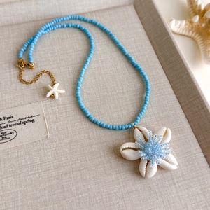 Detailaufnahme einer blauen Perlenkette mit Muschelblüten-Anhänger und kleinem Seestern