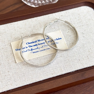 Polished silver metal hoop earrings displayed on a natural linen and wood jewelry tray