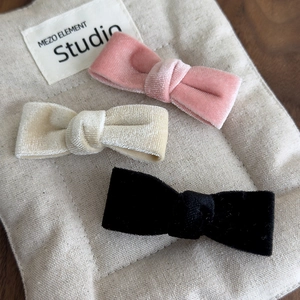 Three-piece velvet bow hair clips set in pink, beige and black displayed on linen fabric