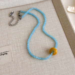 Detail einer blauen Perlenkette mit gelbem Donut-Anhänger und silbernem Karabinerverschluss