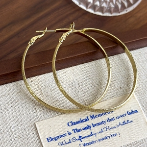 Detailed shot of large golden hoop earrings with textured frost and polished finish