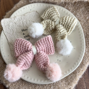 Rosa und beige gestrickte Schleifen-Haarspangen mit flauschigen Pompons auf Teller