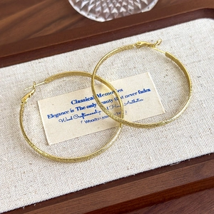 Detailed macro view of large golden hoop earrings with textured frosted metal finish