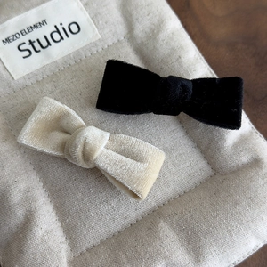 Close-up of black and beige velvet bow hair clips on a soft quilted fabric background