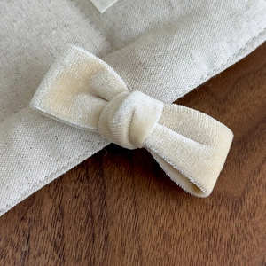 Close-up of cream velvet bow hair clip detail on rustic canvas and wooden surface