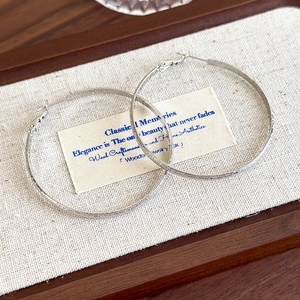 Detail of silver hoop earrings with textured matte finish on a linen wooden tray