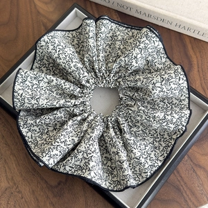 Détail d'un chouchou géant à motif floral avec des feuilles noires et bordure soignée