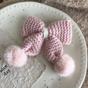 Detail einer rosa gestrickten Haarschleife mit Plüschbommeln auf einem Keramikteller