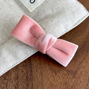 Detail shot of the soft pink velvet bow hair clip on a minimalist wooden surface