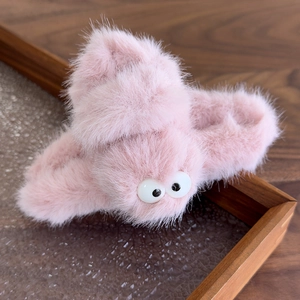 Detail shot of the pink plush hair claw clip with large cute eyes on a wooden tray
