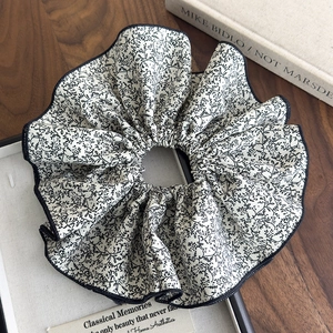 Détail macro du chouchou fleuri beige avec imprimé floral noir délicat sur bois