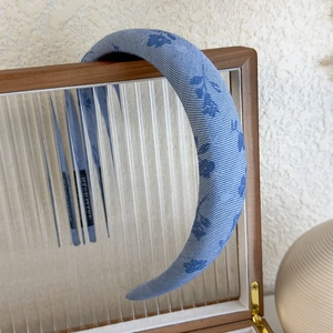 Detail of blue floral checkered headband with thick sponge padding on a wooden stand