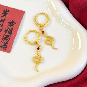 Detail of golden snake hoop earrings with scales and red teardrop gemstone accents