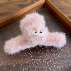 Close-up of pink plush hair claw clip with cartoon big eyes on a wooden texture base