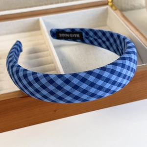 Detail of blue gingham padded headband with handmade label in a wooden display box
