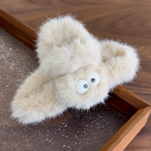 Close-up of a plush beige hair claw clip with big eyes on a wooden background