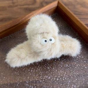 Close-up of soft beige plush hair claw clip with cute big eyes on a wooden tray