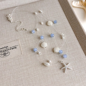 Detail der blauen Perlenkette mit Muscheln und Seestern auf einem beigen Tablett