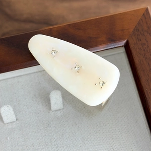 Close-up of vintage cream acetate hair clip with three inlaid rhinestones in a wooden frame