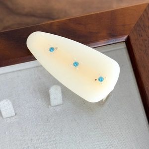 Macro detail of cream acetate hair clip with three inlaid blue rhinestones on a linen lining