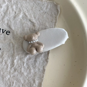 Nahaufnahme der niedlichen 3D Bär Haarklammer mit Perlenkette auf cremefarbenem Stoff